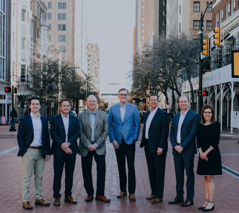 Group photo of the Lacy Malone Ryder & Menefee, PLLC Partners, Associates, and one of the Senior Counsel members standing with the streets of Fort Worth stretching behind them. From left to right, the photo includes: Blake Garcia, David Menefee, Tom Ryder, Justin Malone, Jeff Lacy, Ryan Horner, and ML Menefee.